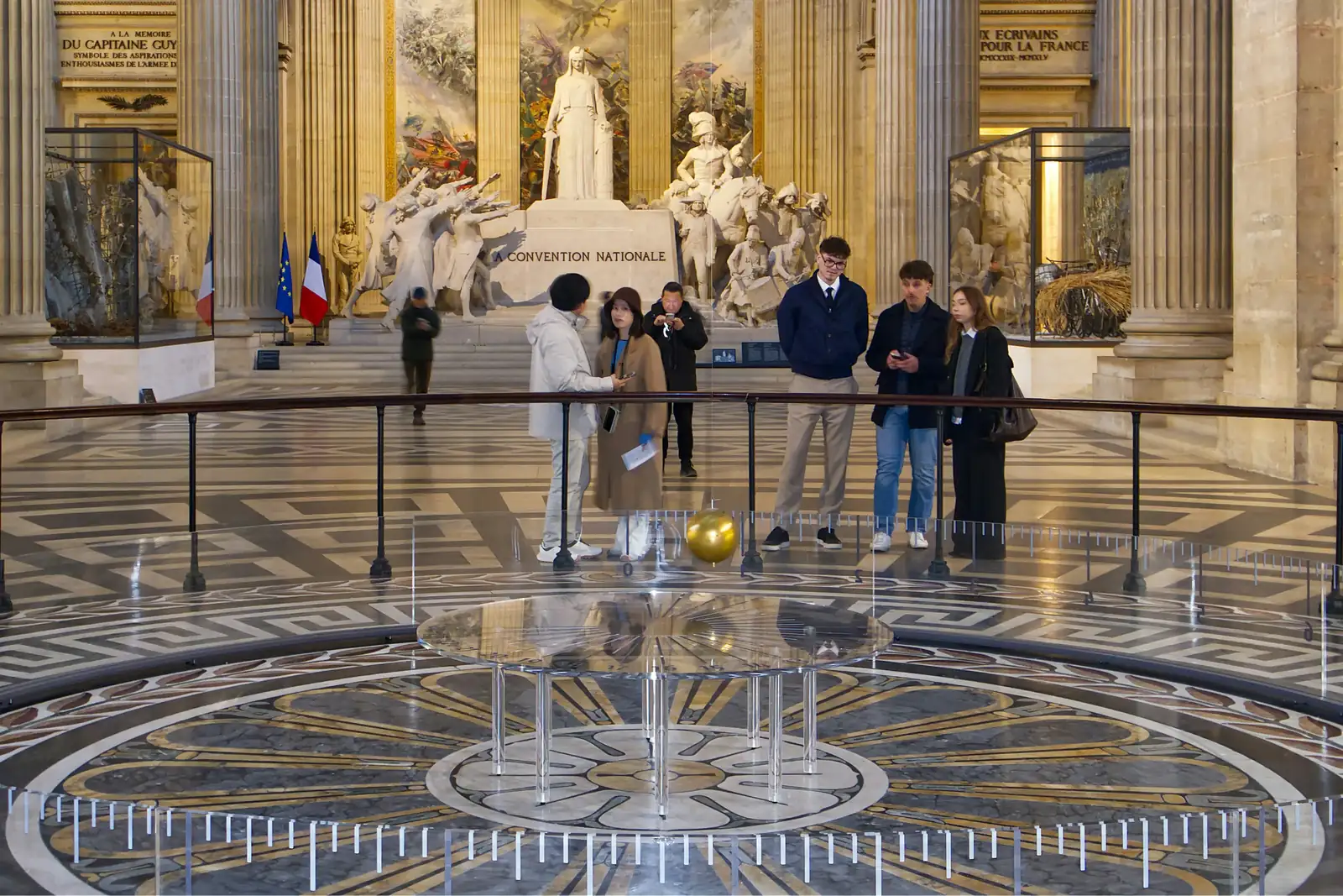 Visitors standing beneath Foucault's pendulum in the nave of the Panthéon, Paris