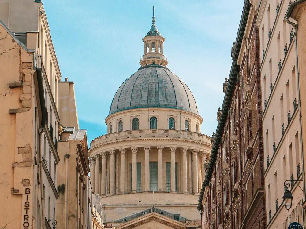 The Panthéon's dome and colonnaded drum framed between the buildings of a Latin Quarter street